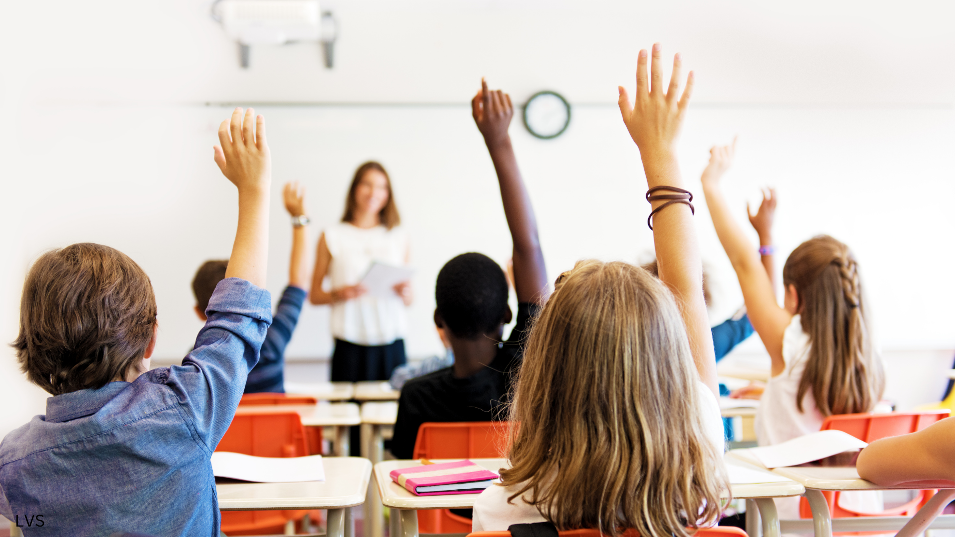 Students raising hands in classroom.