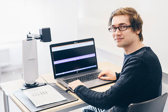 Student using MagniLink S and laptop to read text on desk (laptop not included).