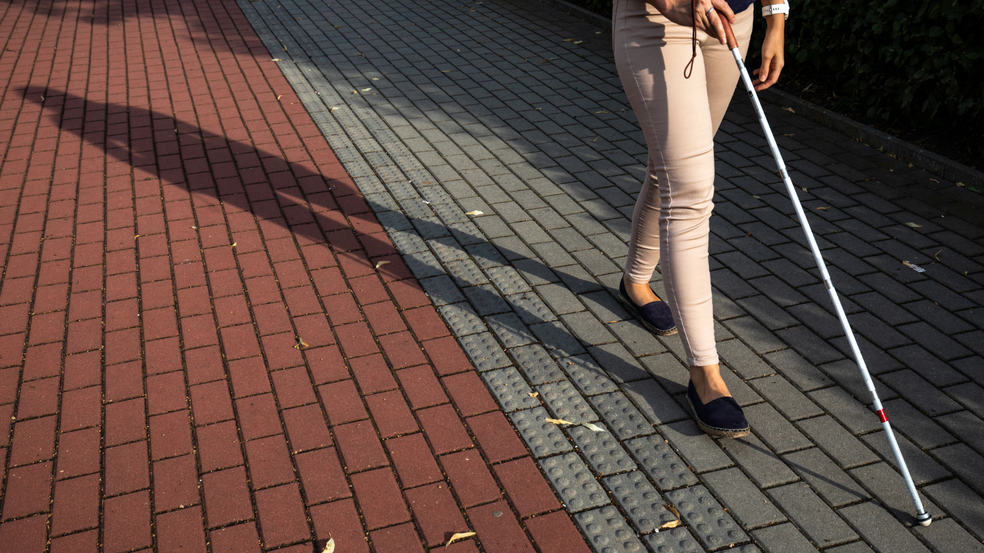 Image of a person using a white mobility cane on a brick sidewalk.