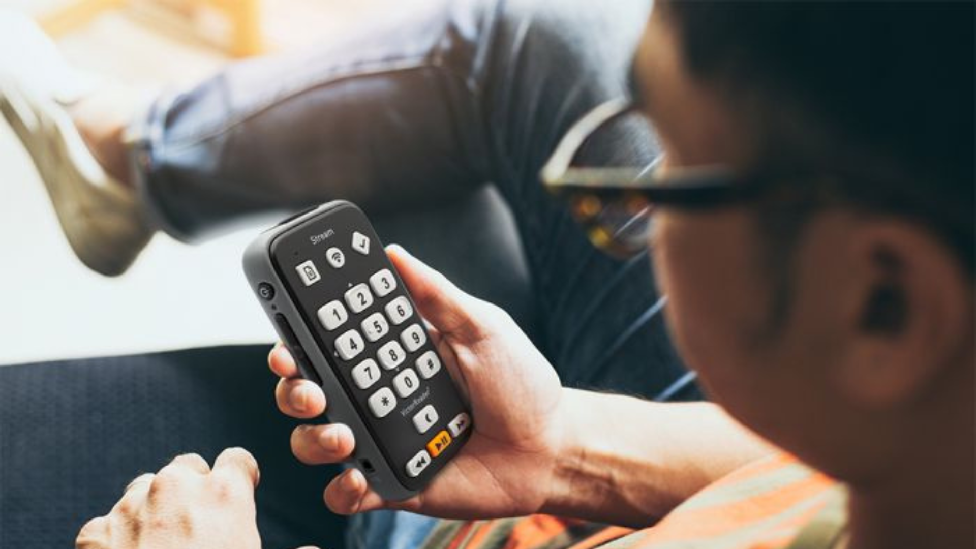 Person wearing glasses holding Victor Reader while sitting at a desk.