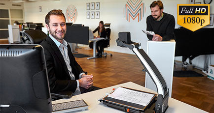 Smiling man using MagniLink Pro at workstation.