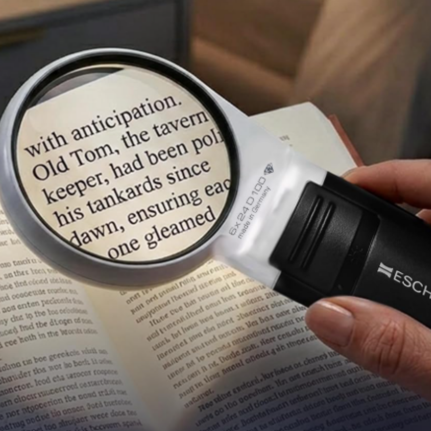 Close up of a hand holding a round magnifying glass that is enlarging text.