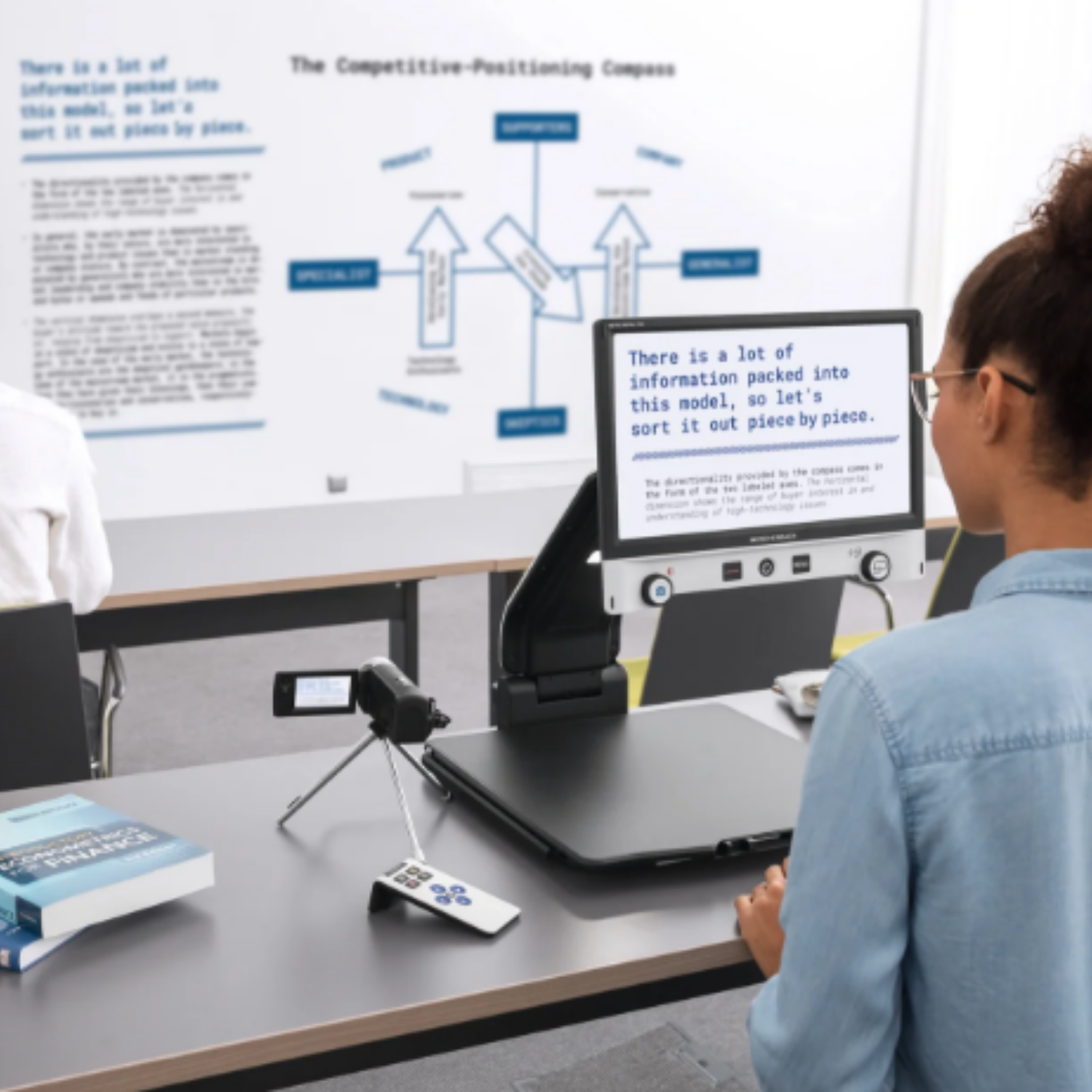 Person standing in front of video magnifier with optional distance camera enlarging white board text.